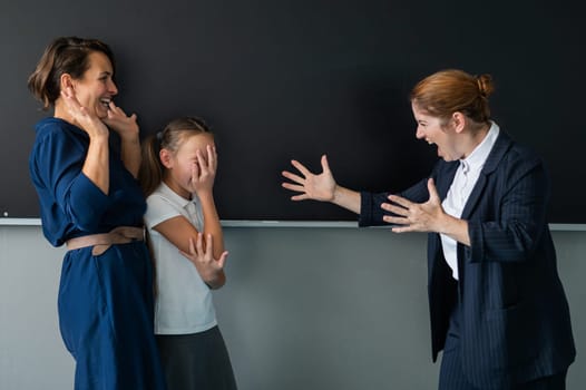 The teacher screams at the schoolgirl and her mother standing at the blackboard
