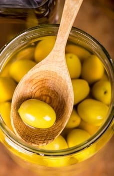 Close up green olives in bank, rosemary on a wooden background