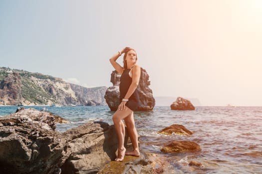 Woman travel sea. Young Happy woman in a long red dress posing on a beach near the sea on background of volcanic rocks, like in Iceland, sharing travel adventure journey