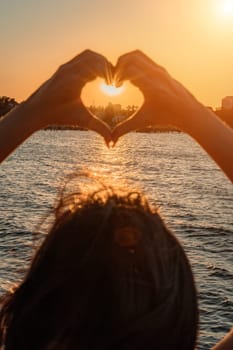 Silhouette against the sunset - hands folded in the shape of a heart. Sun with rays between the palms. Concept for Valentine's Day, declaration of love. Minimalism, space for text, warm colors