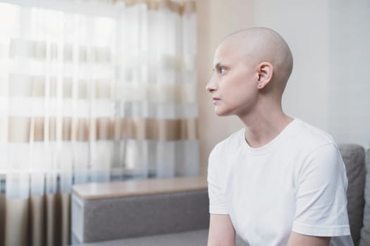 Portrait of a young woman in white t-shirt without hair with a cancer, looks sadly to the window.