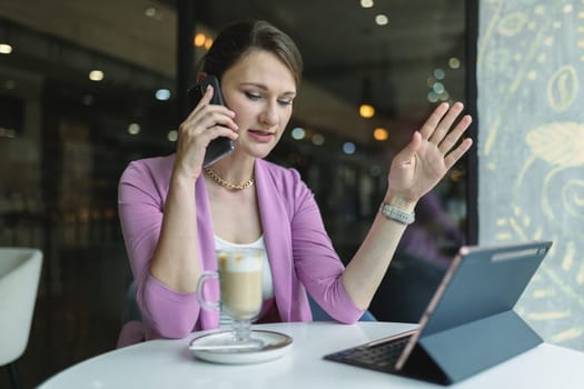 Young business woman solves business issues remotely by phone while sitting in a cafe.