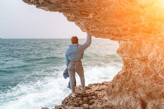 woman sea travel. A woman in a blue jacket stands on a rock above a cliff above the sea, looking at the stormy ocean. Girl traveler rests, thinks, dreams, enjoys nature.