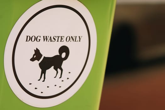A green plastic waste receptacle adorned with a white label specifically designated for dog waste, promoting ecological consciousness and responsible dog excrement disposal.
