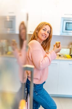 Vertical photo of a caucasian adult woman looking at camera while eating sandwich at home