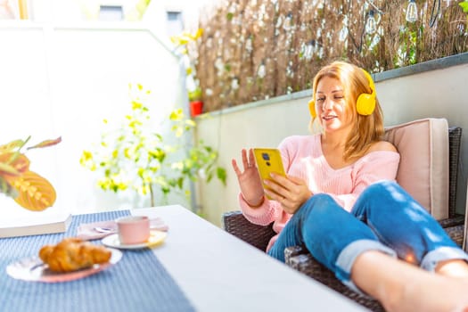 Caucasian adult, woman relaxing at the patio using smart phone and listening to music in the morning