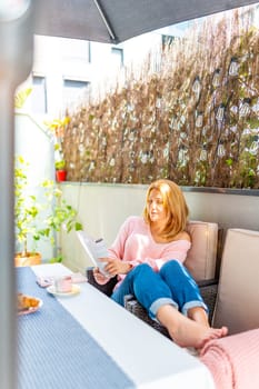 Young relaxed woman reading a book at the patio under the sun