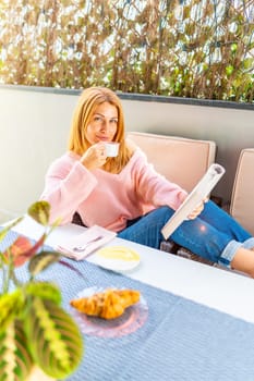 Vertical photo of a caucasian adult woman sipping coffee while reading a book in the yard