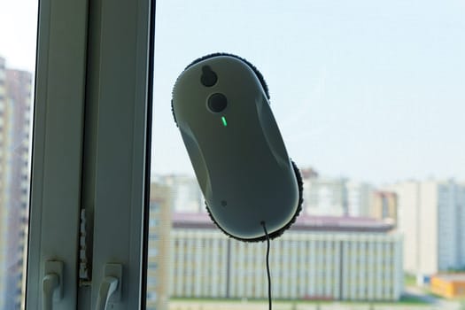 Robotic window cleaner hangs on a window pane, its cord dangling below.
