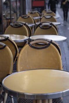 France, Paris - Jan 05, 2024 - Row of Wooden chairs and Steel tables outside a cafe on street in Paris city. Empty outdoor cafe seating area with Yellow chairs and tables, Space for text, Selective focus.