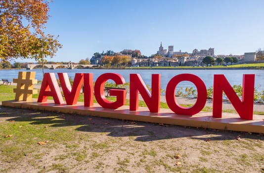 Avignon, France - November 25 2023: Avignon city and his famous bridge photographed with red letters of Avignon sign in the foreground.  Medieval Papal city on the Rhone River