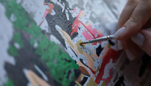 Close-up of woman painting with brush on canvas by numbers. Picture by numbers. Creative hobby or painting for beginners. Leisure activity at home