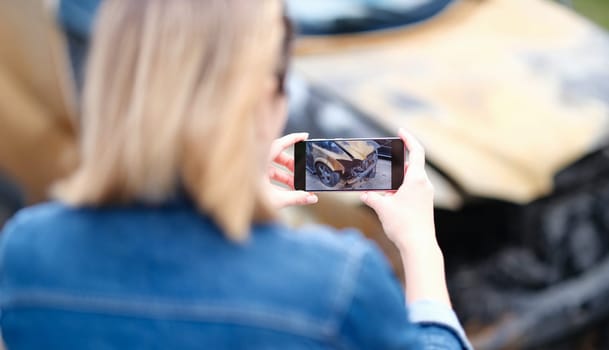 Woman insurance broker making photo of burnt car. Automobile accident and insurance case concept