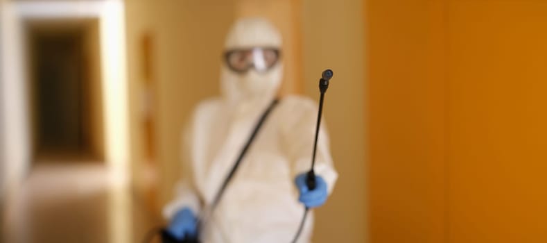 Person in protective suit holding disinfection equipment in hand. Respirator disinfects of apartment with chemical agent, sanitation worker cleans room from coronavirus