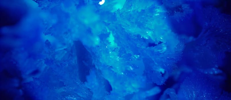 Close-up of frosty drawing in blue colour on window. Winter fairy tale background. Frost backdrop with copy space