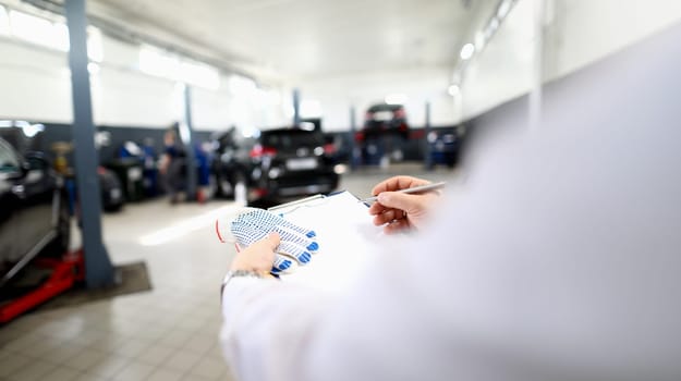 Close-up of male worker writing machine diagnostic data in garage. Fixed car after maintenance in service. Pit stop, service station and handyman concept