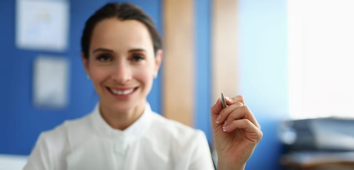 Close-up of smiling woman holding pen and writing in air. Young cheerful office manager drawing something on virtual screen. Advertising or tutoring concept