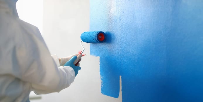 Close-up of painter with brush tool covered in blue colour painting wall. Renovation interior design, construction site and project concept
