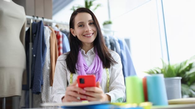 Portrait of female seamstress smiling and posing in sewing workshop. Cheerful female looking at camera with happiness. Designer, art and sewing concept