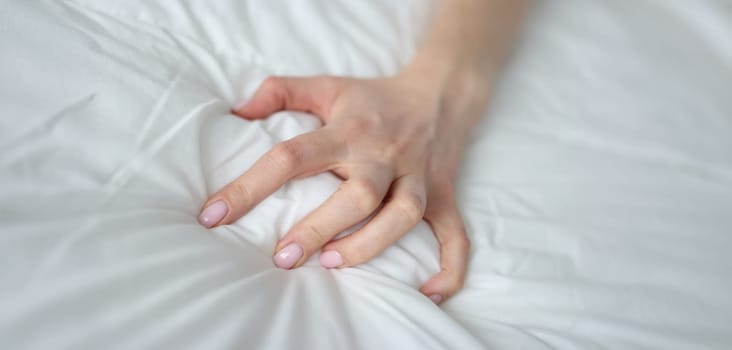 Close-up of sexy female hand pulling and squeezing white sheets in bed. Tender woman hand with sensual manicure. Sexy, pleasure and erotic concept