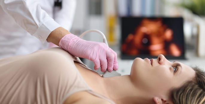 Portrait of doctor endocrinologist doing ultrasound of thyroid gland in clinic. Ultrasound sensor over patients neck with gel. Diagnostics and medicine concept