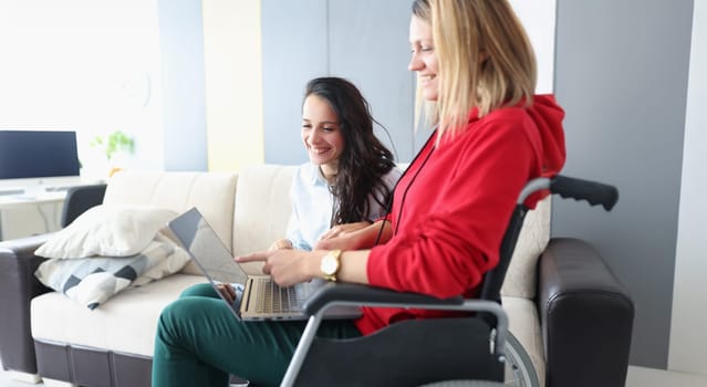 Portrait of smiling friends looking at photos on laptop, woman in wheelchair and disabled people. Pastime together concept