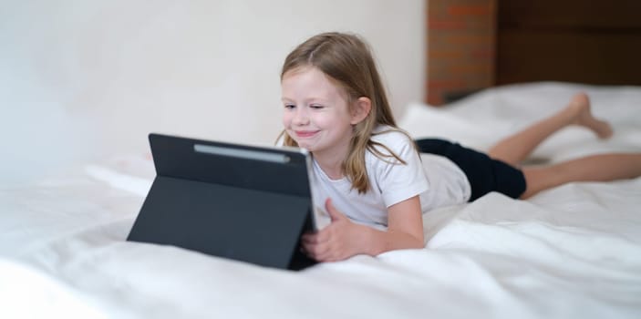 Portrait of smiling cheerful kid having fun with modern tablet. Happy girl having video call with friends or relatives. Happy childhood concept