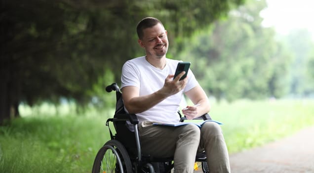 Portrait of man sitting in wheelchair and have communication with friends via video call app. Happy and smiling middle-aged guy. Disability, recovery concept