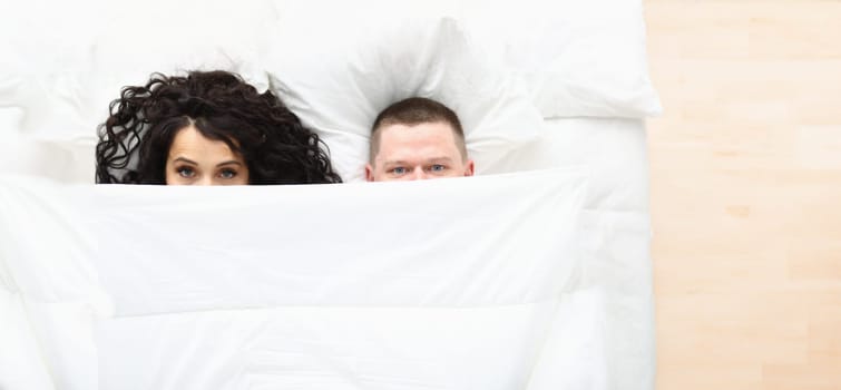 Top view of man and woman covering with white blanket, awake couple in bad. Couple in love hiding under coverlet. Good morning, family and sweet home concept