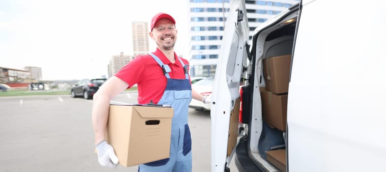 Portrait of smiling courier with parcels near delivery van. Deliveryman holding parcel. Delivery service and receiving packages concept