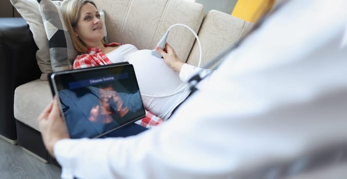 Close-up of gynecologist doing ultrasound scan on belly using modern digital ultrasound machine with tablet. Female patient expecting pregnancy. Gynecology concept