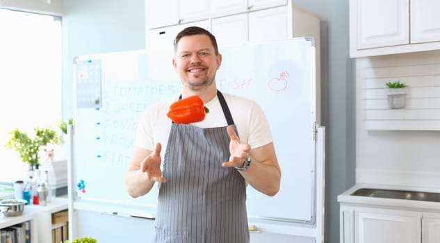 Portrait of smiling male cook catching flying red bell pepper. Man juggling vegetable. Cooking, preparing dish and making content for video blog concept