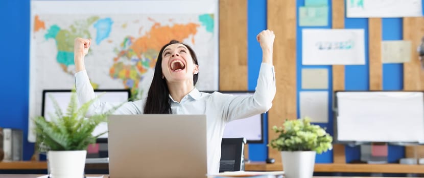Portrait of woman sitting at table in front of computer happy to finish business task, to pass test successfully. Achieve agreement or goal achievement in cooperation