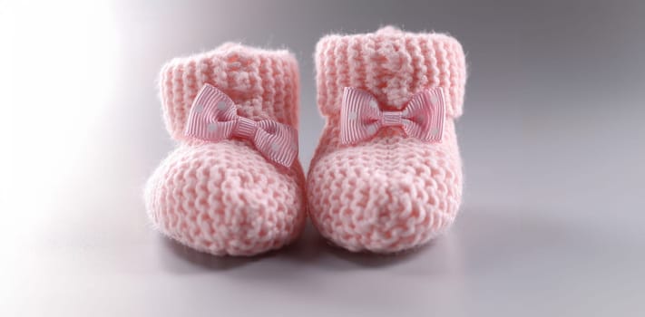 Close-up of handicraft shoes for newborn baby on grey background. Pair of knitted pink baby booties with cute bow. Handmade, preparation for childbirth concept