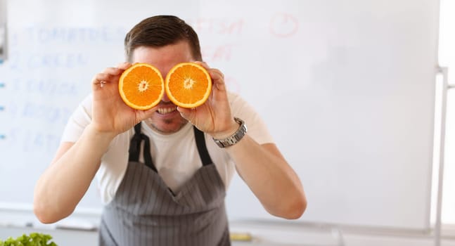 Portrait of man holding cut oranges at eye level instead of glasses. Healthy diet, choose healthy lifestyle and add vitaminized nutrition. Kitchen and raw food diet concept