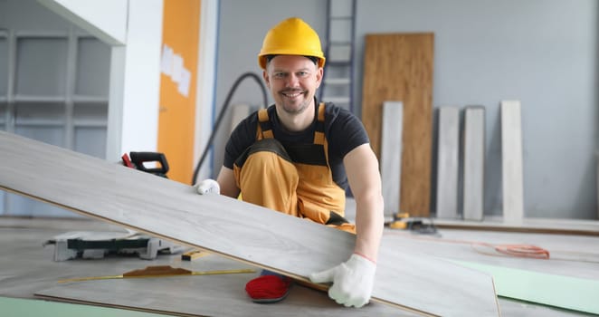 Portrait of professional master overalls making new laminated floor. Man holding wooden tile. Installing laminated floor, interior work and renovation concept