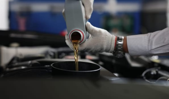 Close-up of auto mechanic refueling and pouring oil into engine motor ia car. Mechanic from maintenance service fix vehicle. Pit stop and car service concept