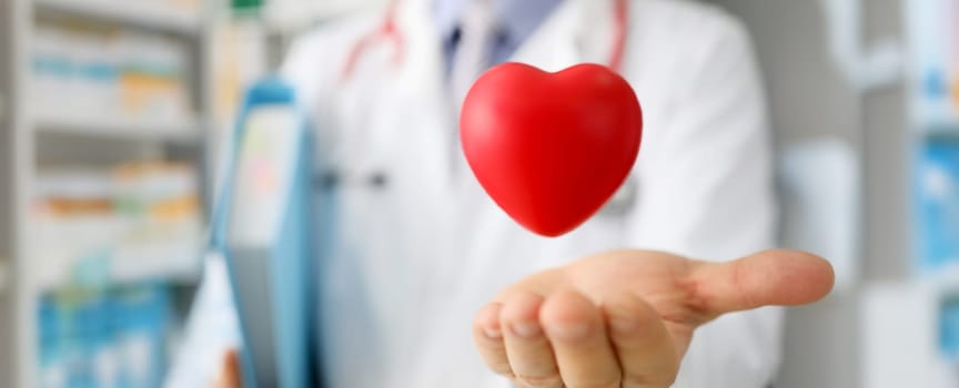 Close-up of doctor hand holding flying red plastic heart heart, save life. Cardiology, medicine, healthcare and prevention of cardiovascular disease concept