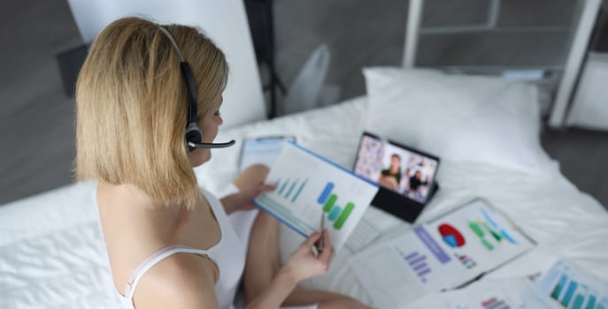 Top view of woman in headset working with documents at home. Business meeting online, distance or remote work. Video conference with colleagues on laptop