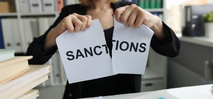 Close-up of woman tearing sheet of paper with sanctions inscription. Reaching an agreement and sanctions cancellation