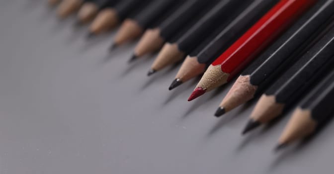 Close-up of one red pencil between row of black pencils. Stand out from crowd, not like everyone else and individuality concept