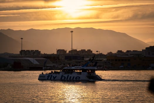 Spain Malaga 1 28 2024 Sunset maritime scene featuring 'Fly Blue' boat, silhouetted cityscape, warm tones and radiant sky download image