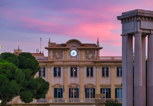 European-style Spain building with clock, bathed in warm sunrise sunset light, amidst green trees and grand architecture. download image