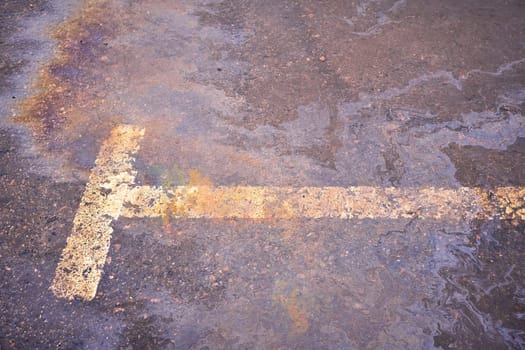 Oil spill on wet asphalt, parking lot with dividing line.