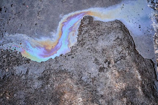 Leakage of oil or gasoline from a car on wet asphalt on a bright sunny day. Abstract background.