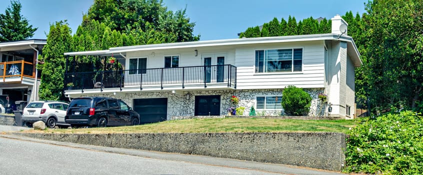 Average family house on land terrace with concrete retaining wall and cars parked on the driveway