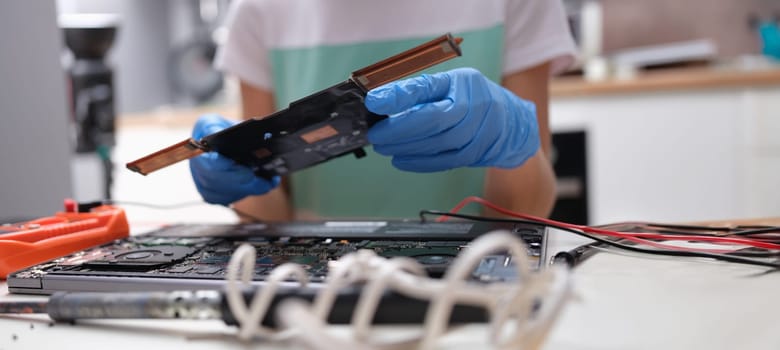 Close-up of tech fixes motherboard of laptop in service center. Laptop disassembling parts and devices