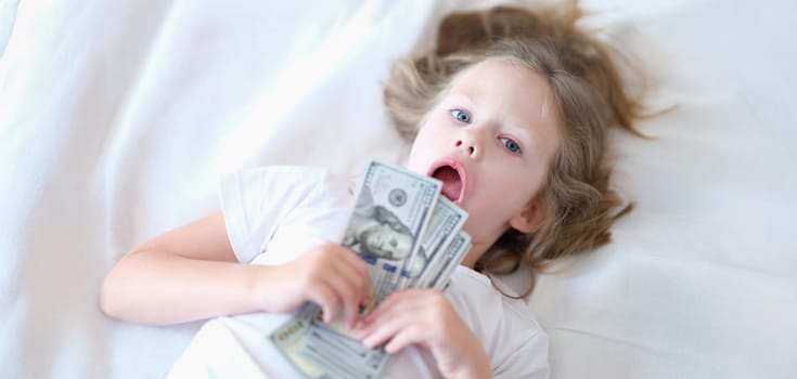 Portrait of small cheerful girl holding cash in hands. Little smiling child counting money, happy childhood.