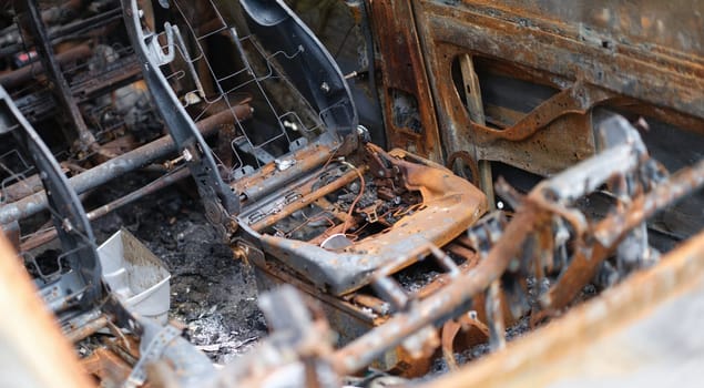 Close-up of car after fire, iron parts of burnt vehicle. Riot, civil protest, hooliganism, criminal in city. Explosion fire result. Car insurance concept