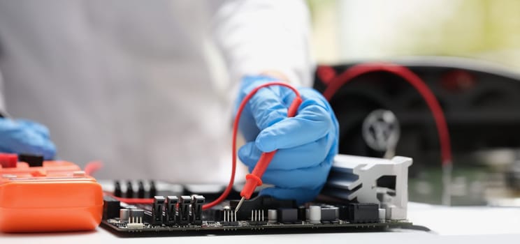 Close-up of technician measuring voltage of in computer mainboard using electronic digital multimeter. Computer hardware, repairing and upgrade